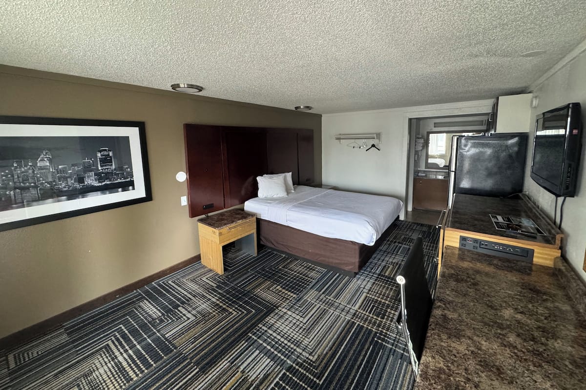 Una habitación de hotel con una cama, un escritorio, un televisor y un cuadro en la pared.