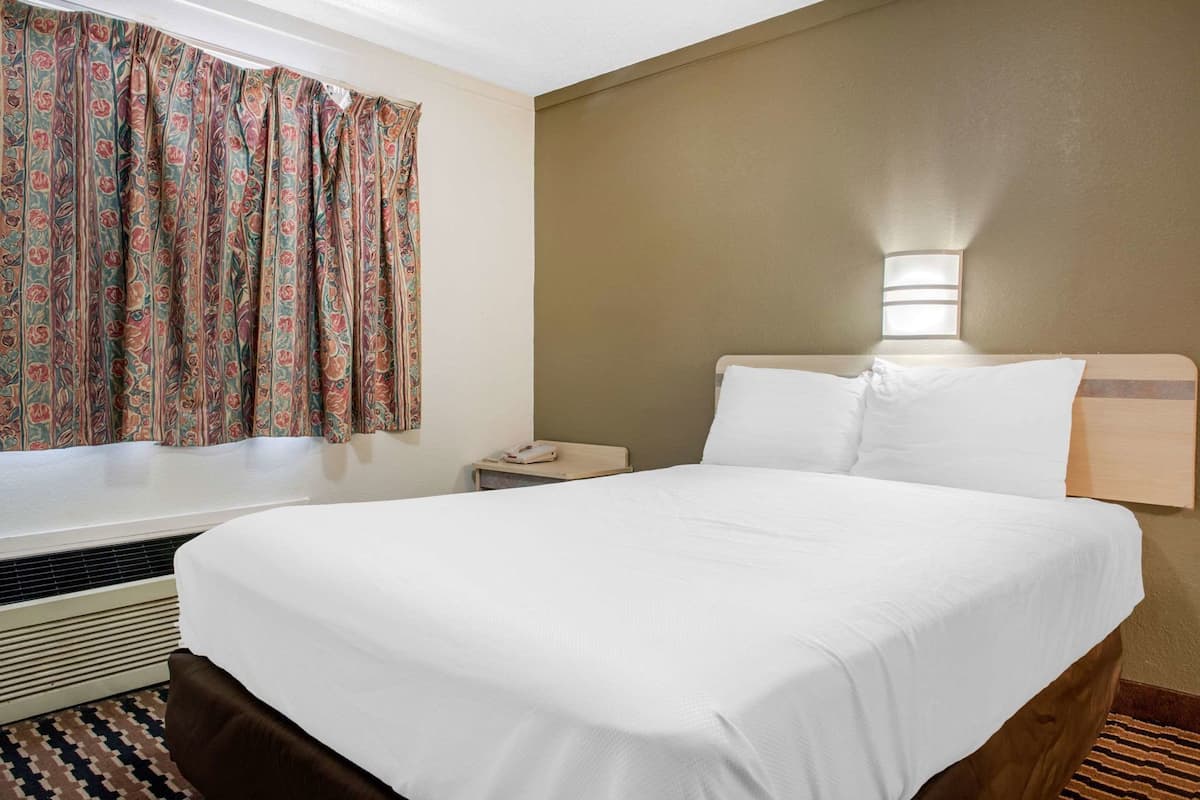 Habitación de hotel con una cama grande, una mesita de noche con lámpara, una ventana con cortinas estampadas y un radiador.