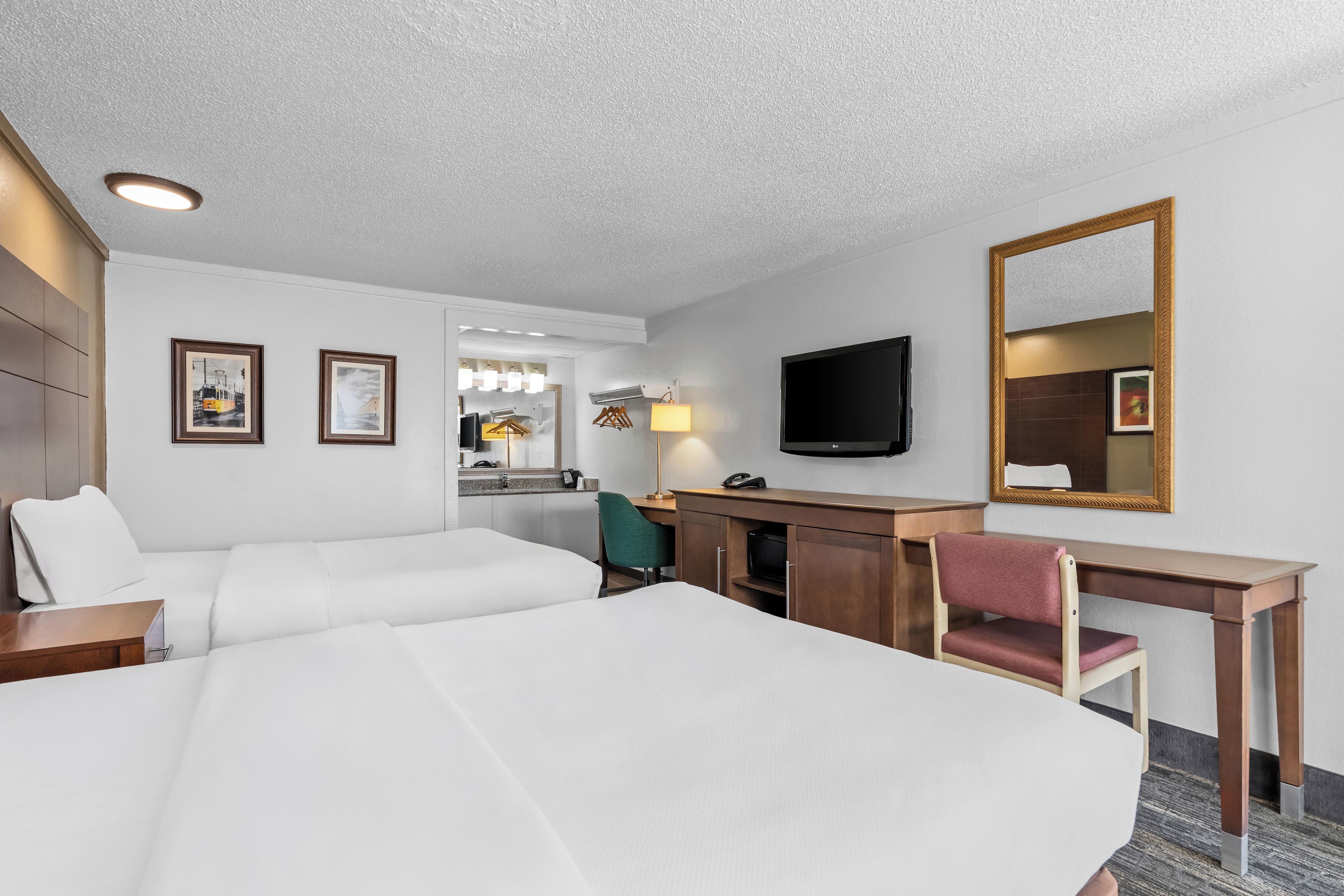 Una habitación de hotel con una cama grande, un escritorio con una silla, un televisor y un espejo.