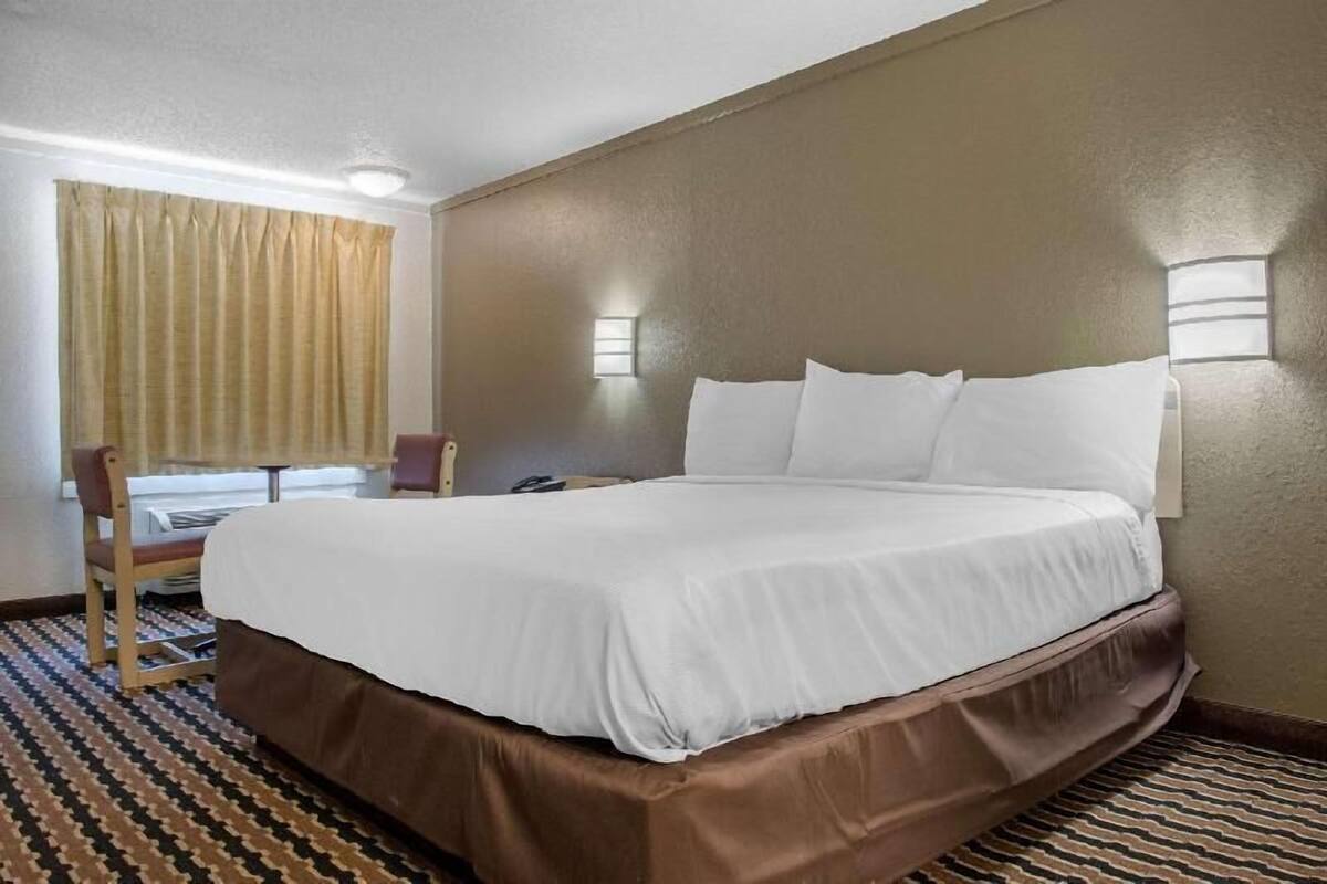 Una habitación de hotel con una cama grande, una silla, una mesita y una ventana con cortinas.