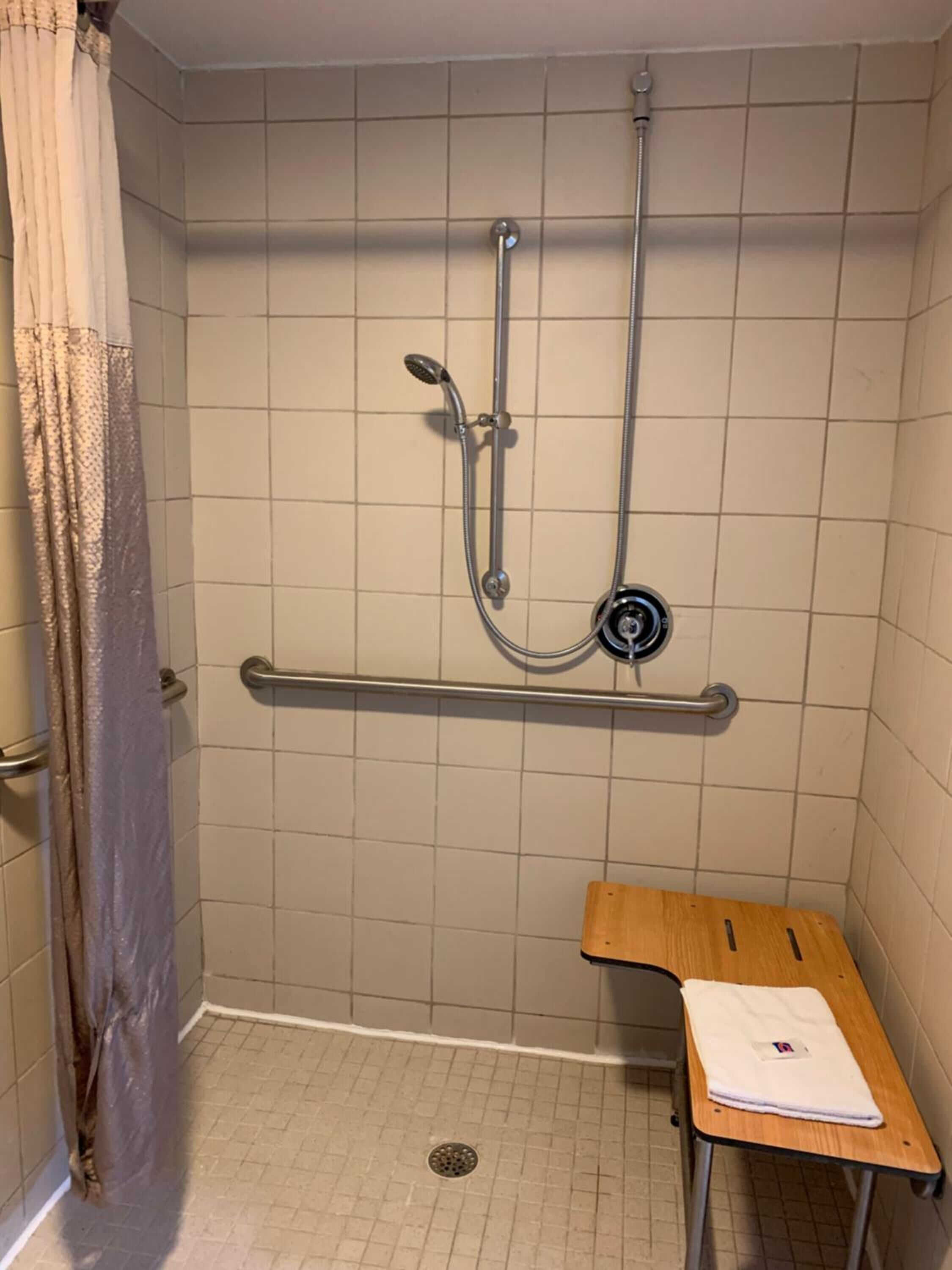 A small, enclosed shower area with a grab bar, a wooden bench, and a showerhead.