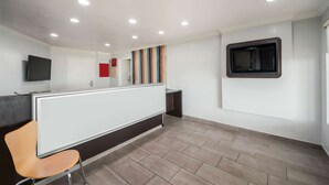 A modern reception area with a reception desk, a television mounted on the wall, and a striped wall decoration. - Motel 6 Laredo, TX - North I-35 (Laredo)