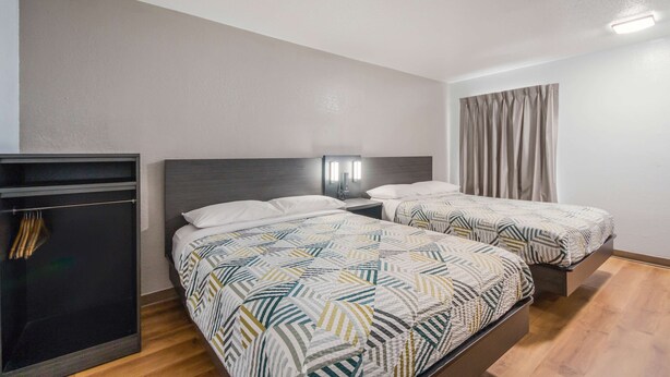 A hotel room with two beds, a wardrobe, and a nightstand with a lamp. - Motel 6 Laredo, TX - North I-35 (Laredo)