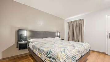 Una habitación de hotel moderna con una cama grande, una mesita de noche con lámpara y una ventana con cortinas.