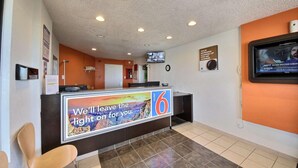 A hotel reception area with a counter displaying a sign, a television mounted on the wall, and a clock. - Motel 6 Laredo, TX - North I-35 (Laredo)