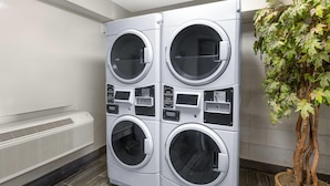 A four-door front-loading washer and dryer unit with control panels and a vent below. - Travelodge by Wyndham Madison Heights MI (Madison Heights)