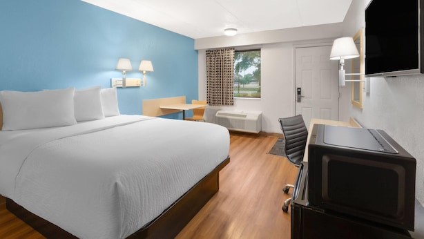 A hotel room with a bed, a desk, a chair, a TV, and a window with curtains. - Travelodge by Wyndham Madison Heights MI (Madison Heights)