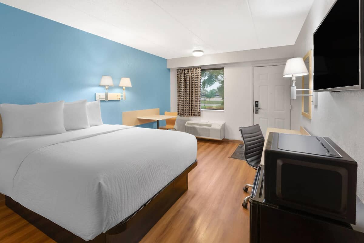 Habitación de hotel con cama, escritorio, silla, televisor y ventana con cortinas.