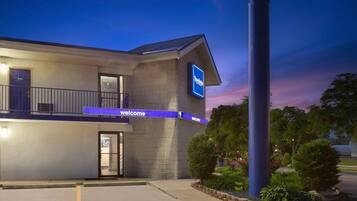 A modern hotel with a 'Welcome' sign, a balcony, and a well-maintained garden area.