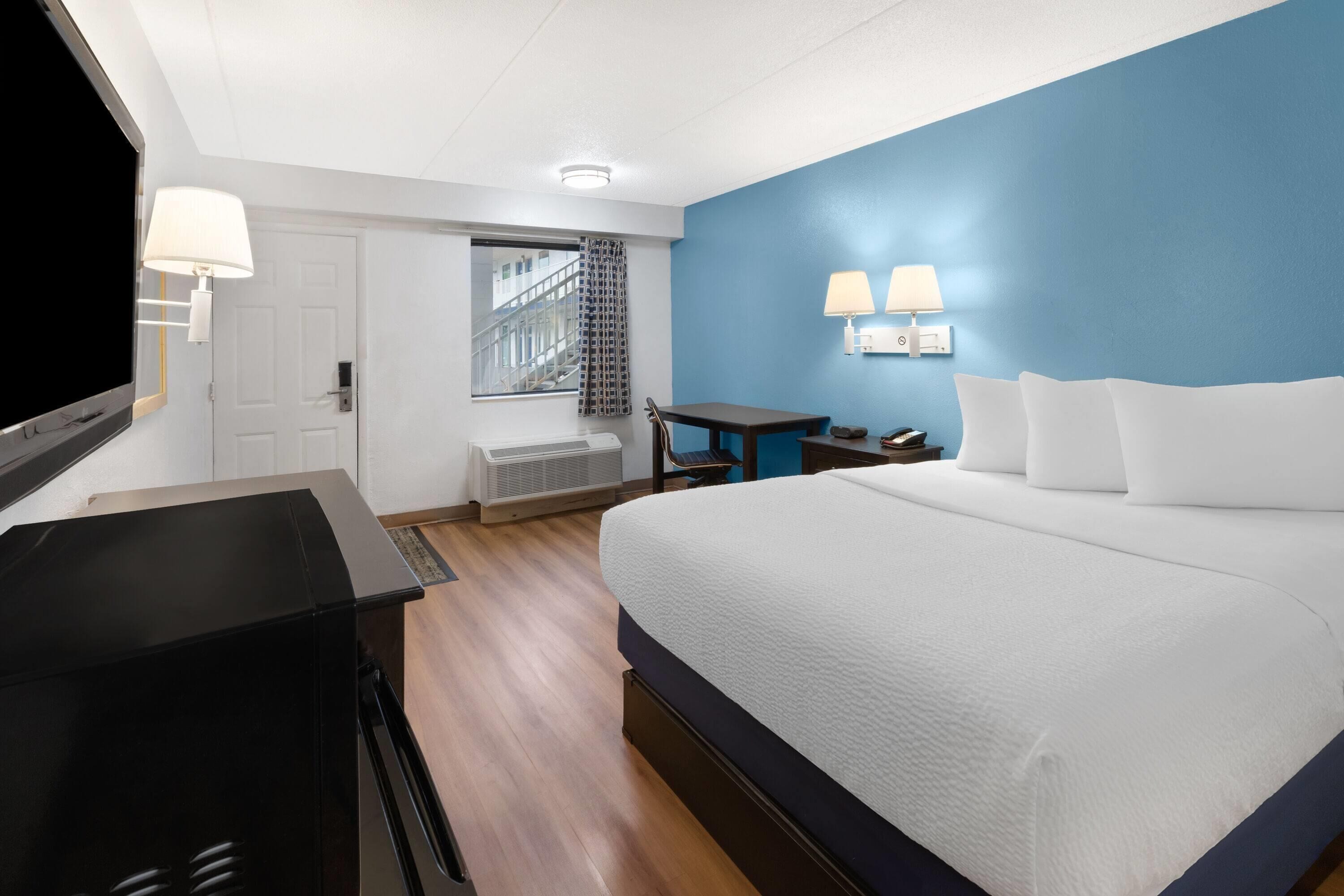A hotel room with a large bed, a desk with a chair, a TV, and a window with a view of the outside.