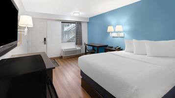 A hotel room with a large bed, a desk with a chair, a TV, and a window with a view of the outside.