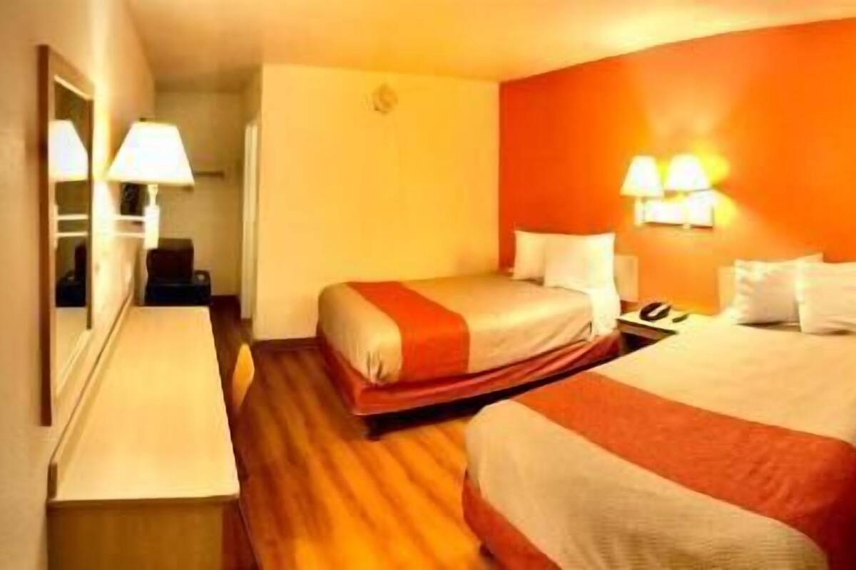 Una habitación de hotel con dos camas, un escritorio y un espejo.