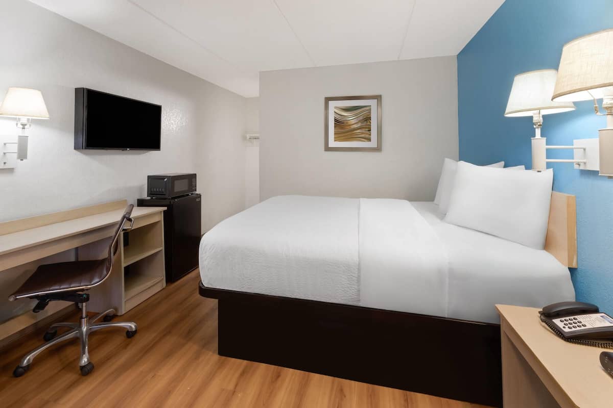 Una habitación de hotel con cama, escritorio, silla, televisor y teléfono en una mesita de noche.