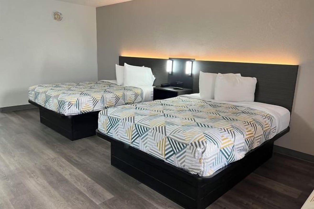A hotel room with two beds, each with a patterned bedspread, a dark headboard, and bedside lamps.