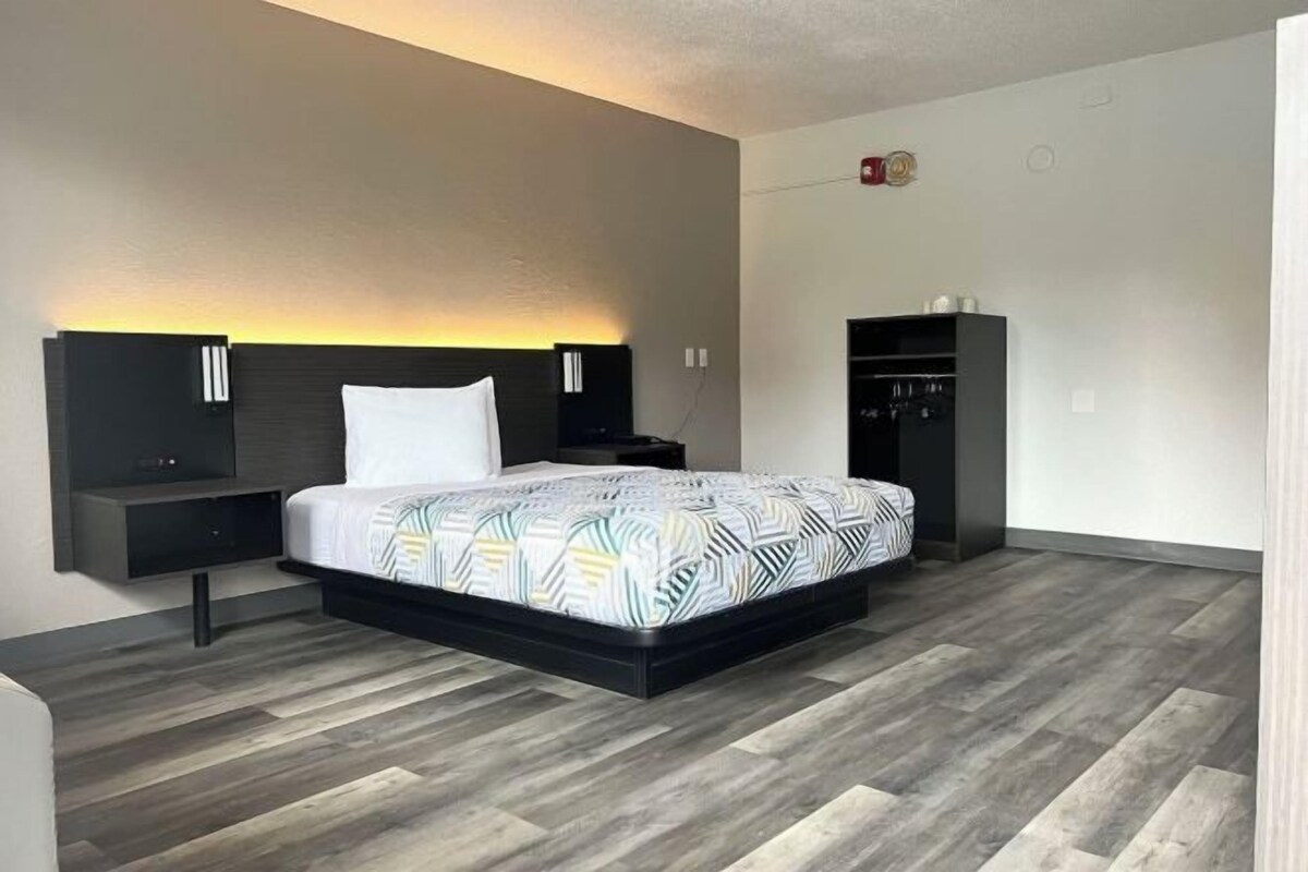 A modern hotel room with a large bed, bedside tables, a wardrobe, and a wall-mounted light fixture.