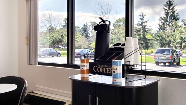 A coffee station with a coffee maker, cups, and a sign indicating freshly brewed coffee. - Motel 6 Middleburg Heights, OH - Cleveland (Middleburg Heights)