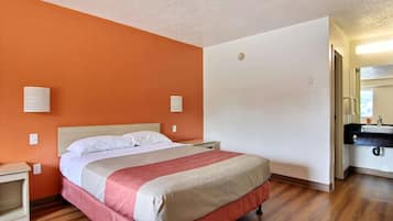 Une chambre d’hôtel comprenant un lit, une table de chevet, une salle de bain avec un lavabo et un miroir.