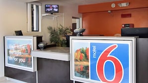 A reception desk with a digital screen displaying a message, a sign indicating room number 6, and a television mounted on the wall. - Motel 6 Middleburg Heights, OH - Cleveland (Middleburg Heights)