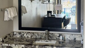 A bathroom with a large mirror, a granite countertop, a towel rack, and a window with a view of buildings. - Days Inn by Wyndham Charleston WV (Charleston)