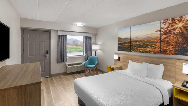 A hotel room with a large bed, a desk, a chair, a TV, a window with curtains, a painting, and a lamp. - Days Inn by Wyndham Charleston WV (Charleston)