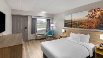Een hotelkamer met een groot bed, een bureau, een stoel, een televisie, een raam met gordijnen, een schilderij en een lamp.