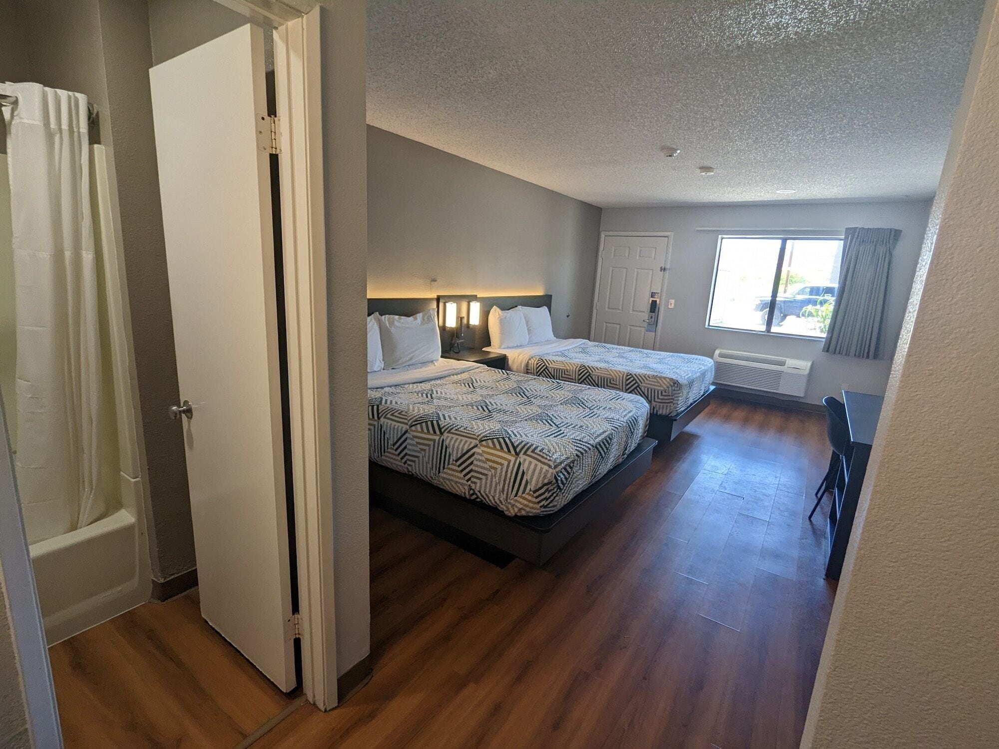 A hotel room with two beds, a bathroom, and a view of the outside.