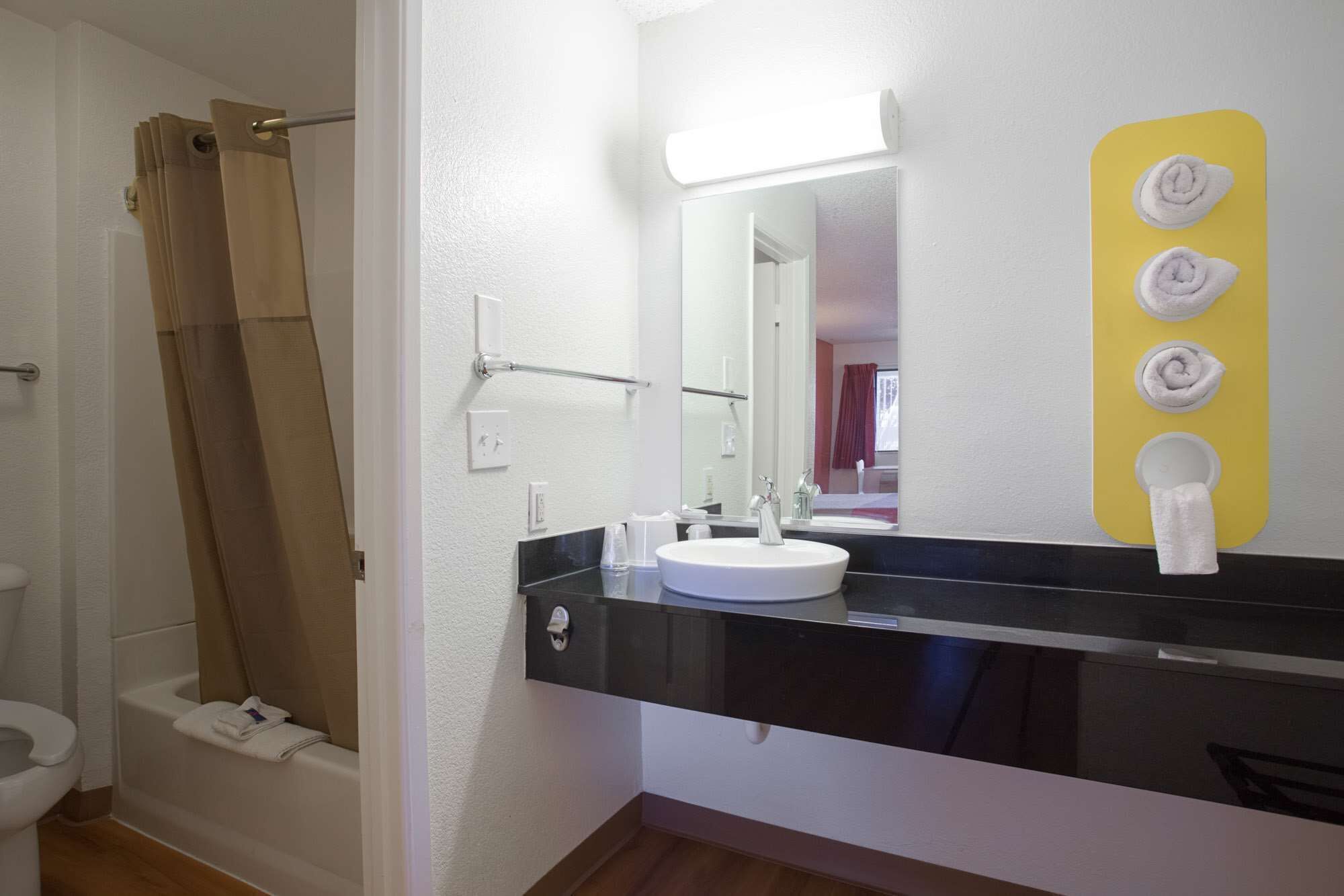 A bathroom with a white sink, black countertop, and a mirror. There is a towel rack with towels and a shower curtain.