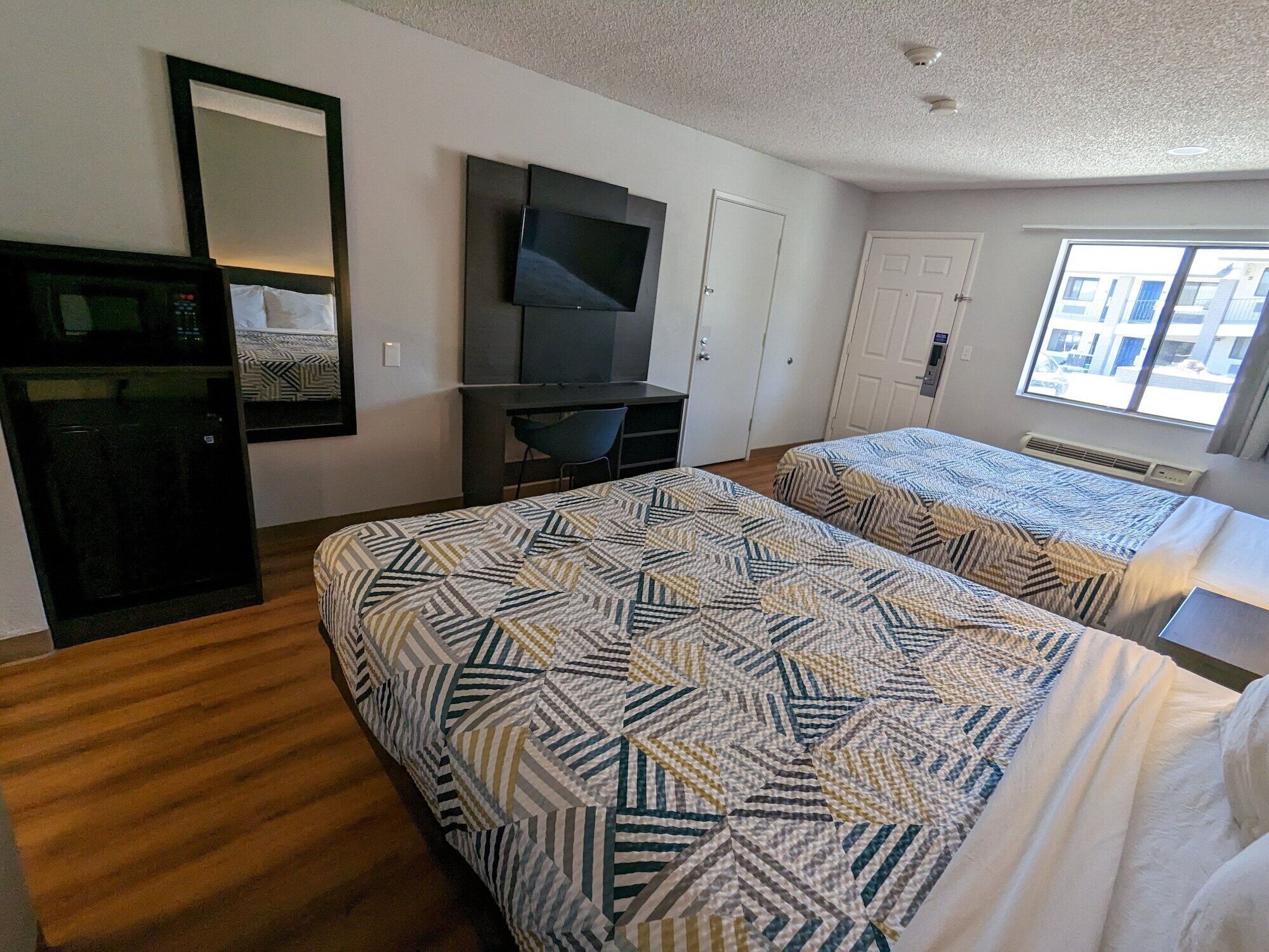 A hotel room with two beds, a TV, a desk, and a window.