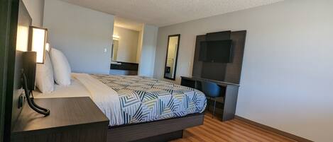A hotel room with a bed, bedside table, lamp, desk, chair, TV, and a mirror.