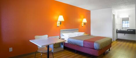 Una habitación de hotel con una cama, lámparas de noche, un escritorio y una silla.