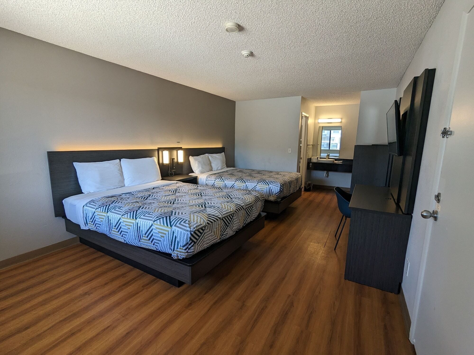 A hotel room with two beds, a desk, a mirror, and a TV.