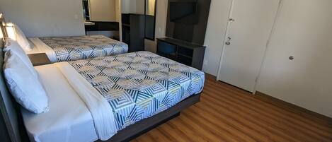 A hotel room with two beds, a TV, a mirror, and a door.