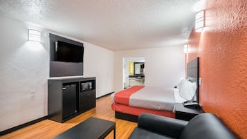 Una habitación de hotel compacta con cama, escritorio, televisor y kitchenette.