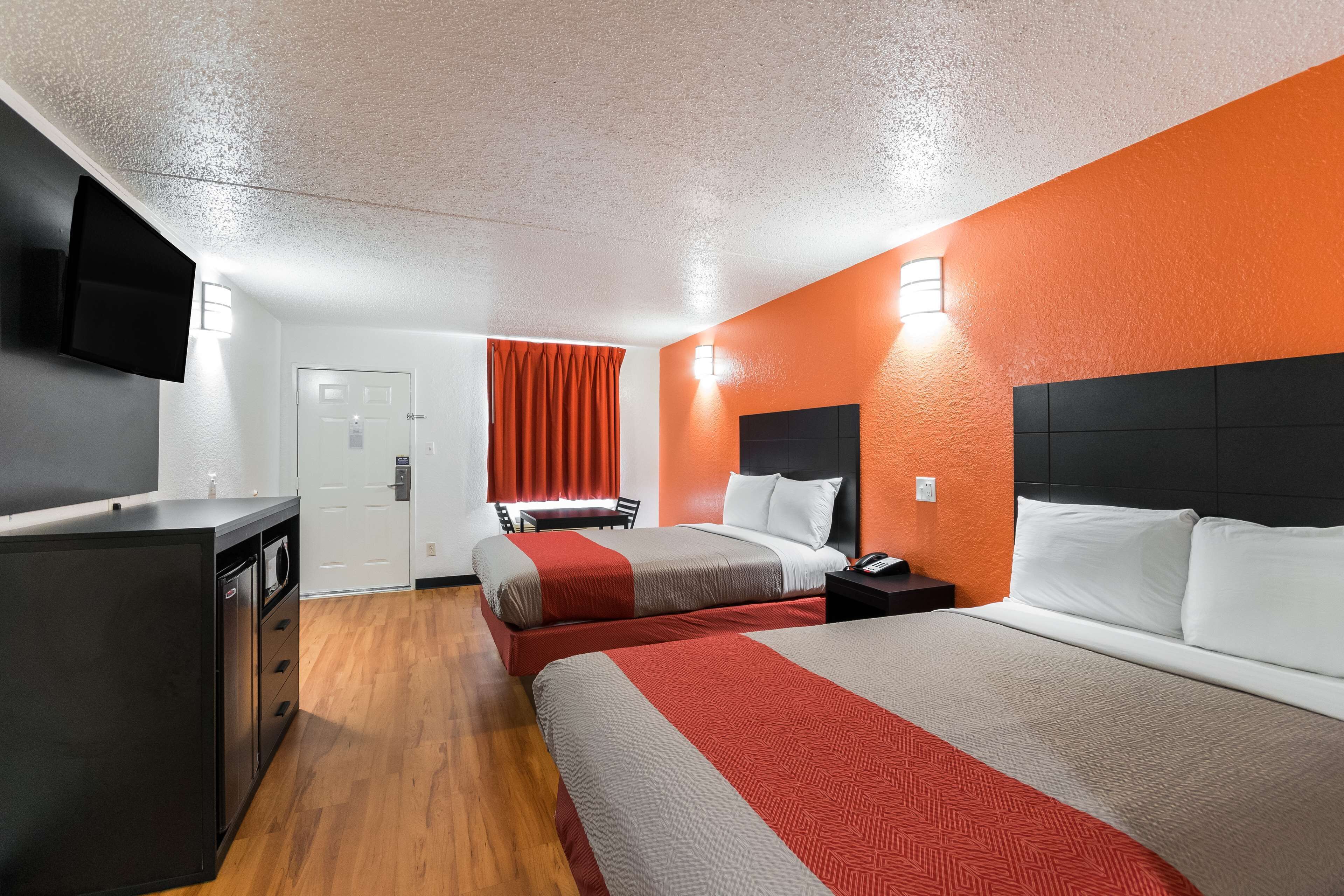 A hotel room with a bed, bedside table, TV, and a desk with drawers.