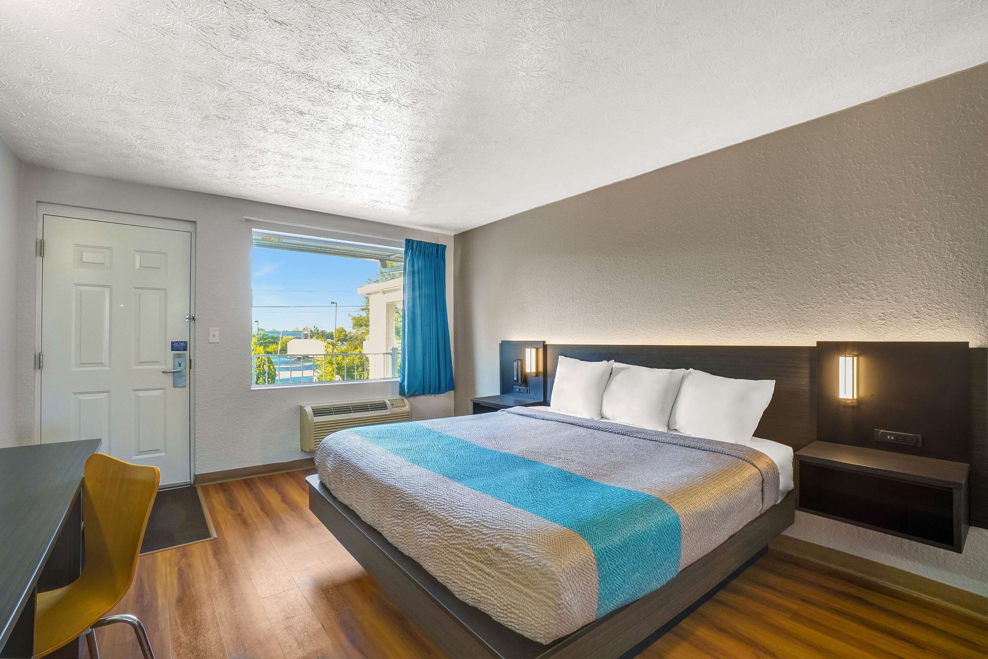 Ein Hotelzimmer mit einem großen Bett, einem Schreibtisch, einem Stuhl, einem Fenster mit Blick und einem Nachttisch mit Lampe.