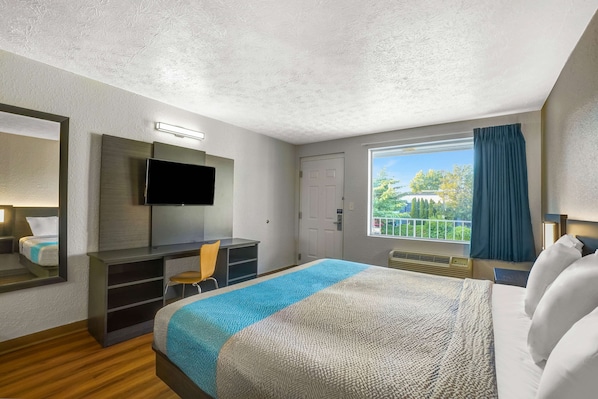 A hotel room with a bed, a desk, a chair, a TV, and a window with a view of greenery. - Motel 6 Lexington I-75 Hamburg (Lexington)