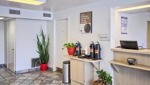 A reception area with a desk, a coffee machine, a trash bin, and a potted plant. - Motel 6 Lexington I-75 Hamburg (Lexington)