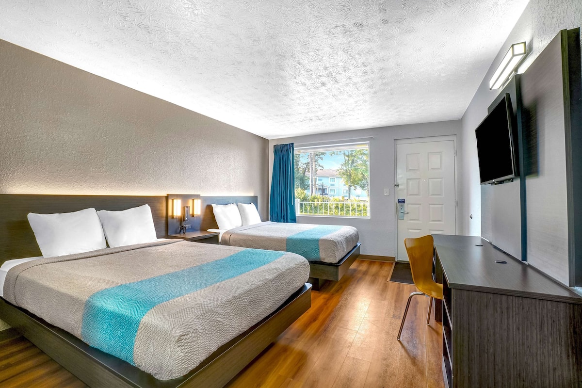 A hotel room with two beds, a desk, a TV, and a window with curtains.