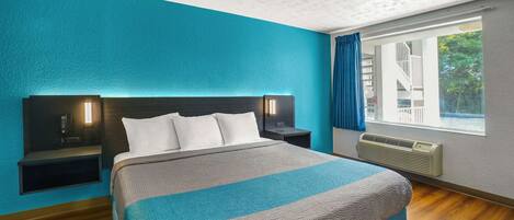 Quarto de hotel moderno com uma cama grande, duas mesas de cabeceira, uma janela com cortinas e vista para o exterior.