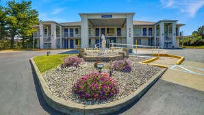 A motel with a 'welcome' sign, a central fountain, and a parking lot with a landscaped garden. - Motel 6 Lexington I-75 Hamburg (Lexington)