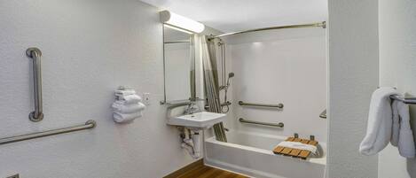 A modern bathroom with a wooden floor, a white sink, a shower with a glass door, and handrails.