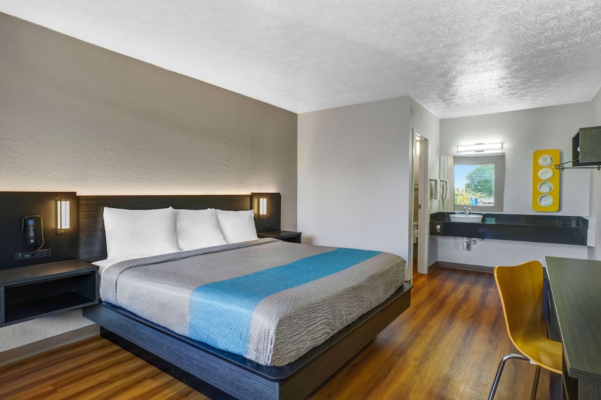 A modern hotel room with a bed, bedside table, and a small desk with a chair.