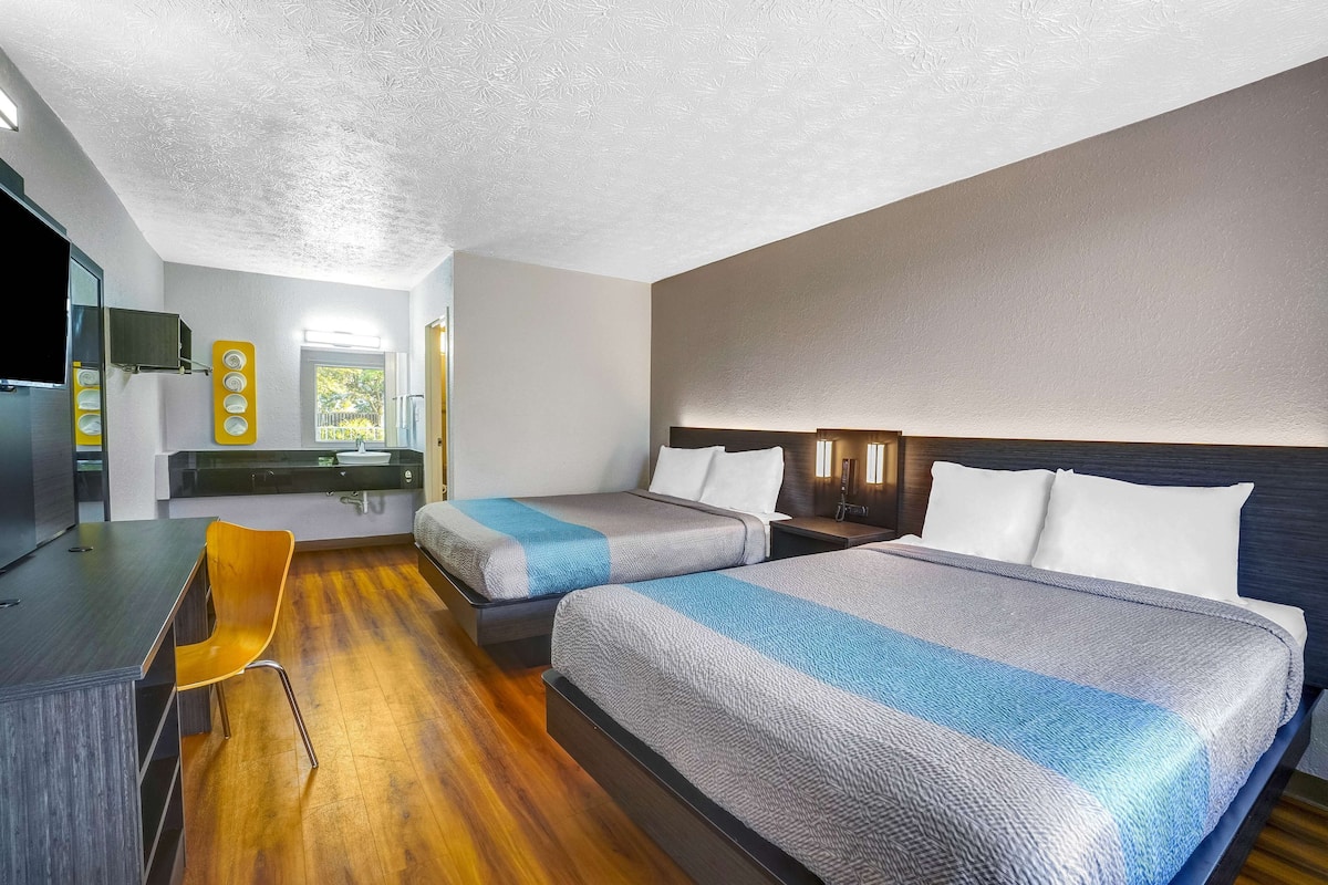 A hotel room with two beds, a desk, a chair, and a TV.