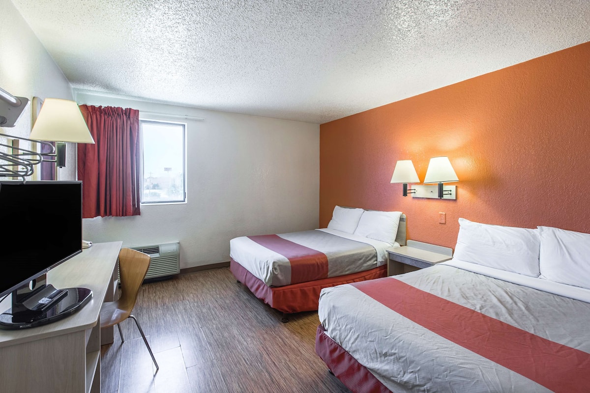 A hotel room with two beds, a desk with a computer, a TV, and a window with curtains.