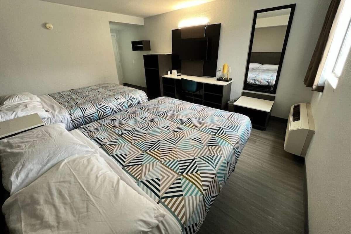 A hotel room with two beds, a desk, a chair, a mirror, and a window.