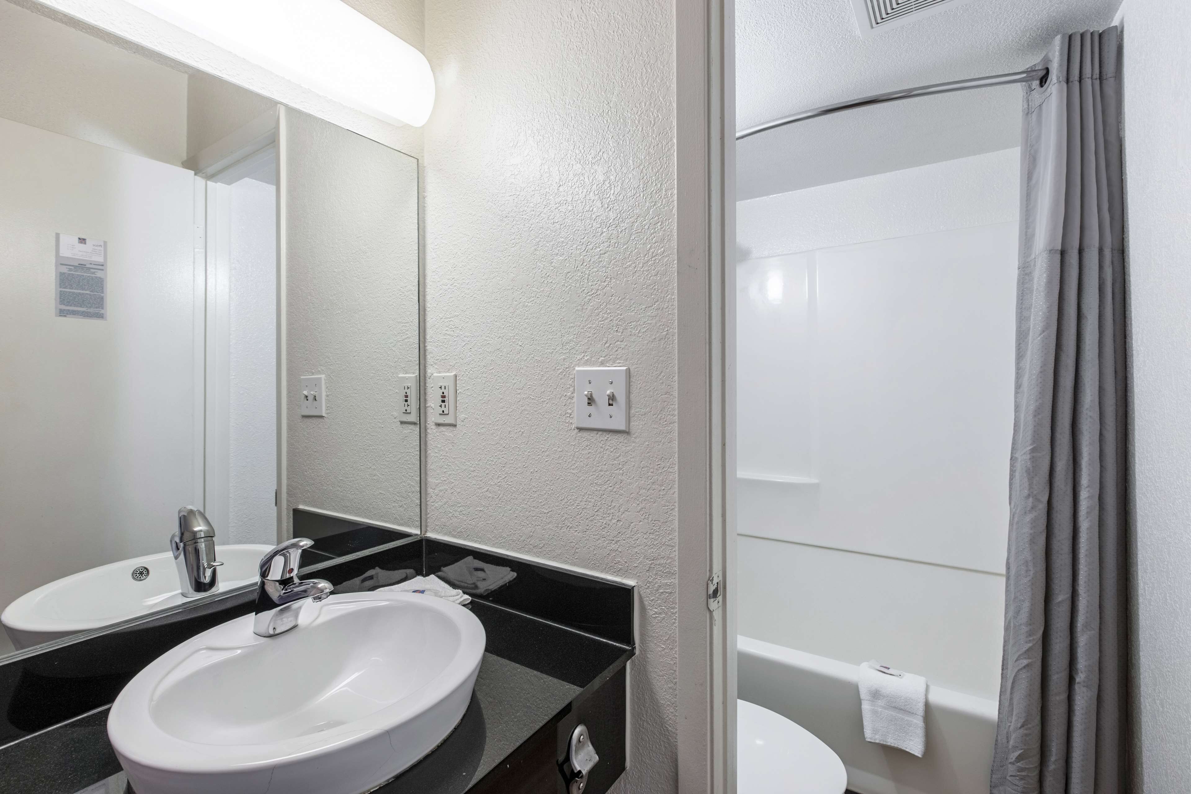 A bathroom with a white sink, a mirror, a black countertop, a shower curtain, and a white toilet.