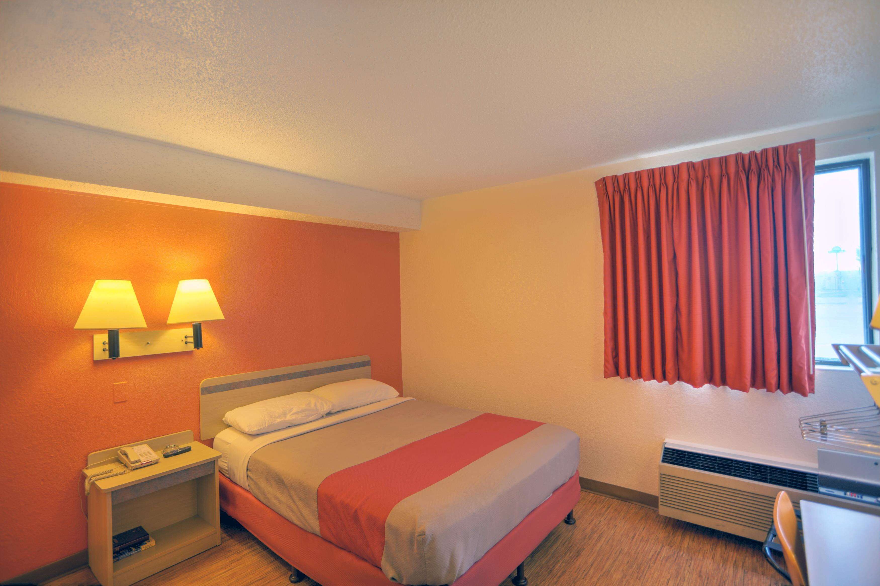 Una habitación de hotel con cama, lámparas de noche, escritorio y ventana con cortinas.