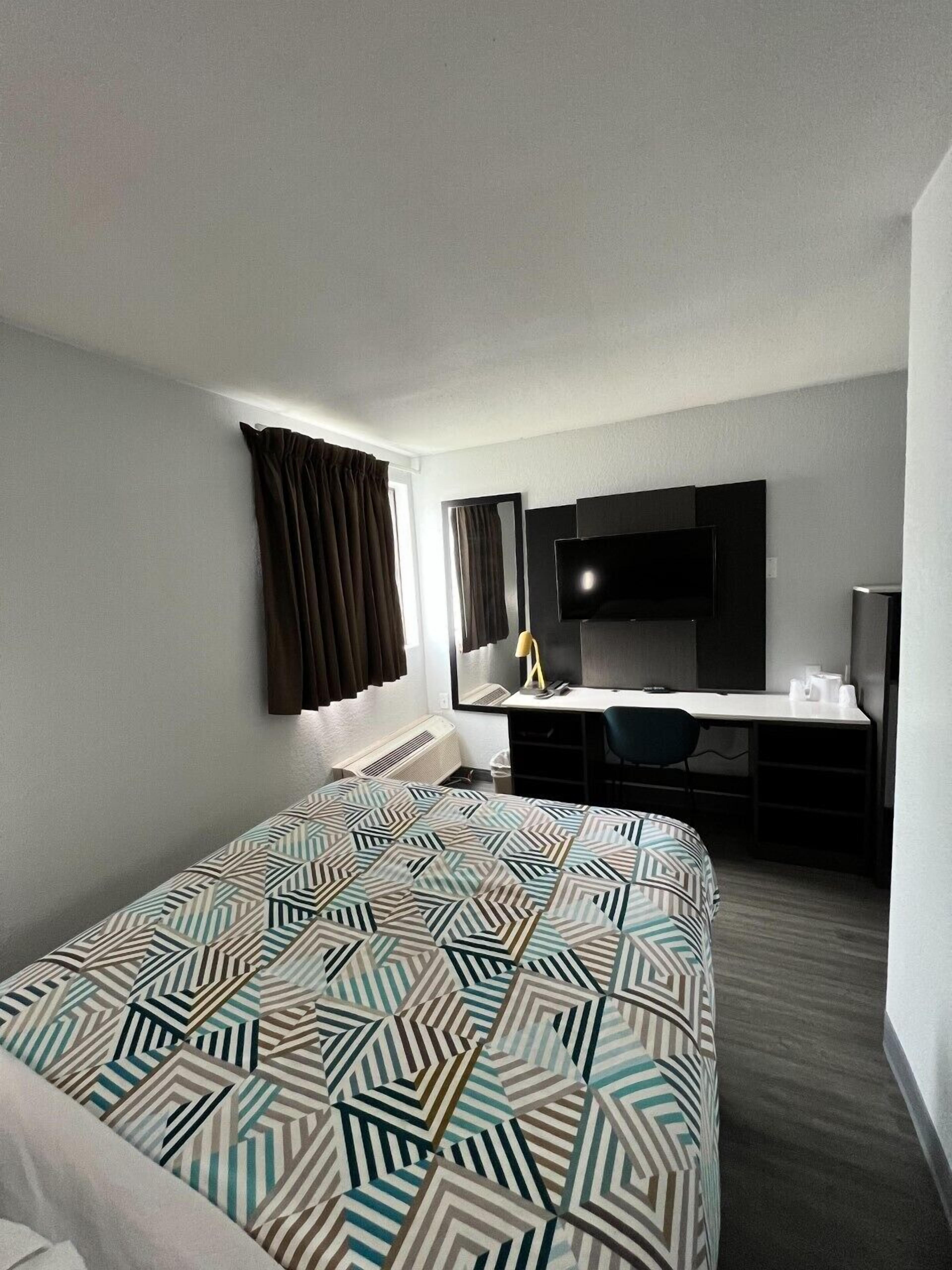 A hotel room with a bed, a desk, a chair, a television, and a window with curtains.