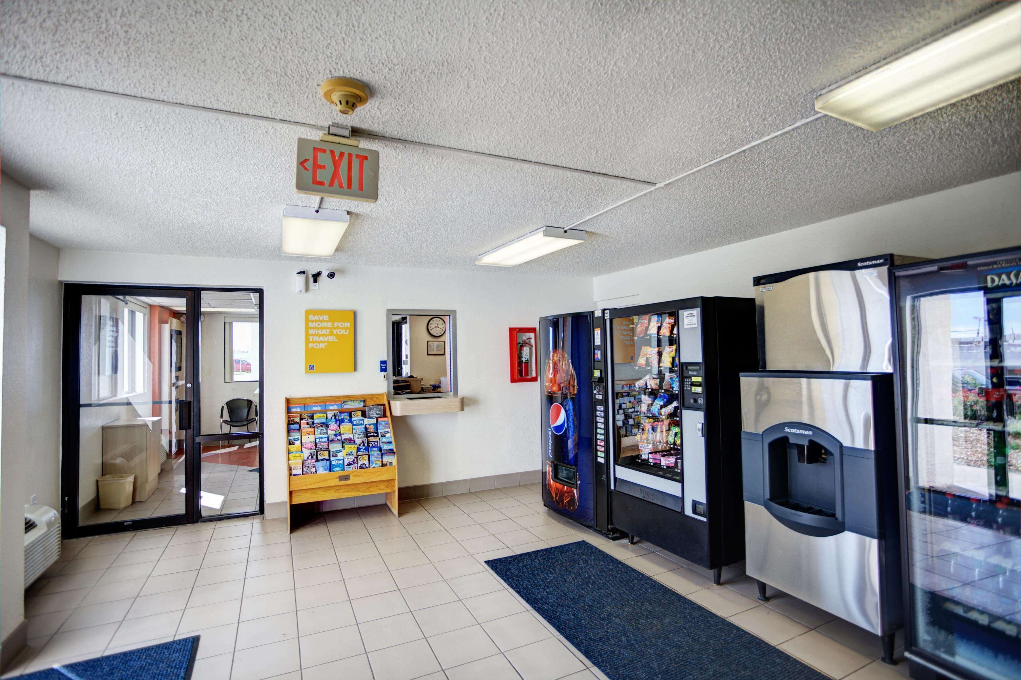 A lobby with an exit sign, vending machines, a clock, and a small display stand.