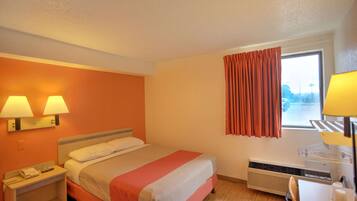 A hotel room with a bed, two bedside lamps, a heater, a window with curtains, and a desk with a lamp.